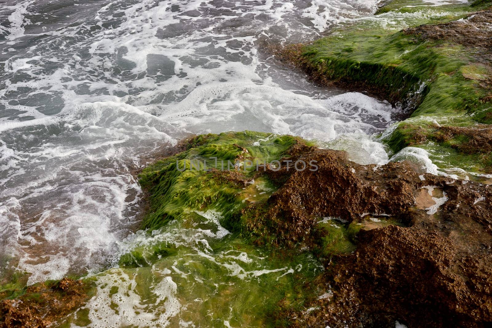 A rocky beach with seaweed and waves lapping on it by raul_ruiz