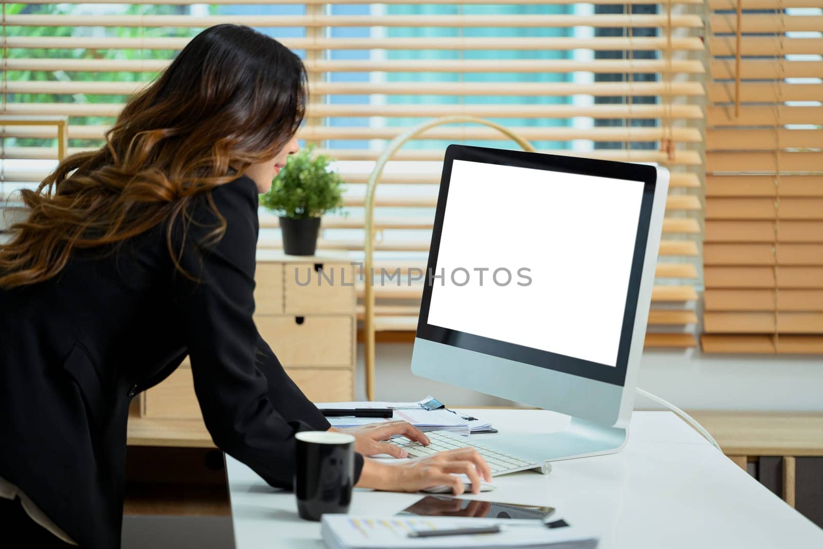 Side view of businesswoman standing in her office and working with computer by prathanchorruangsak