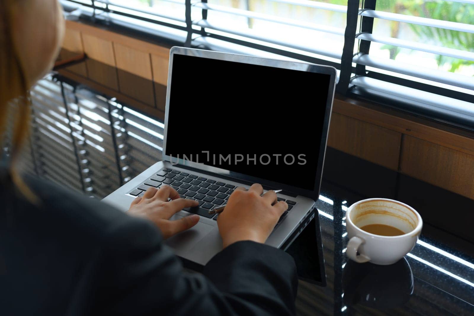 Over shoulder view of businesswoman using laptop on table at modern coffee shop by prathanchorruangsak