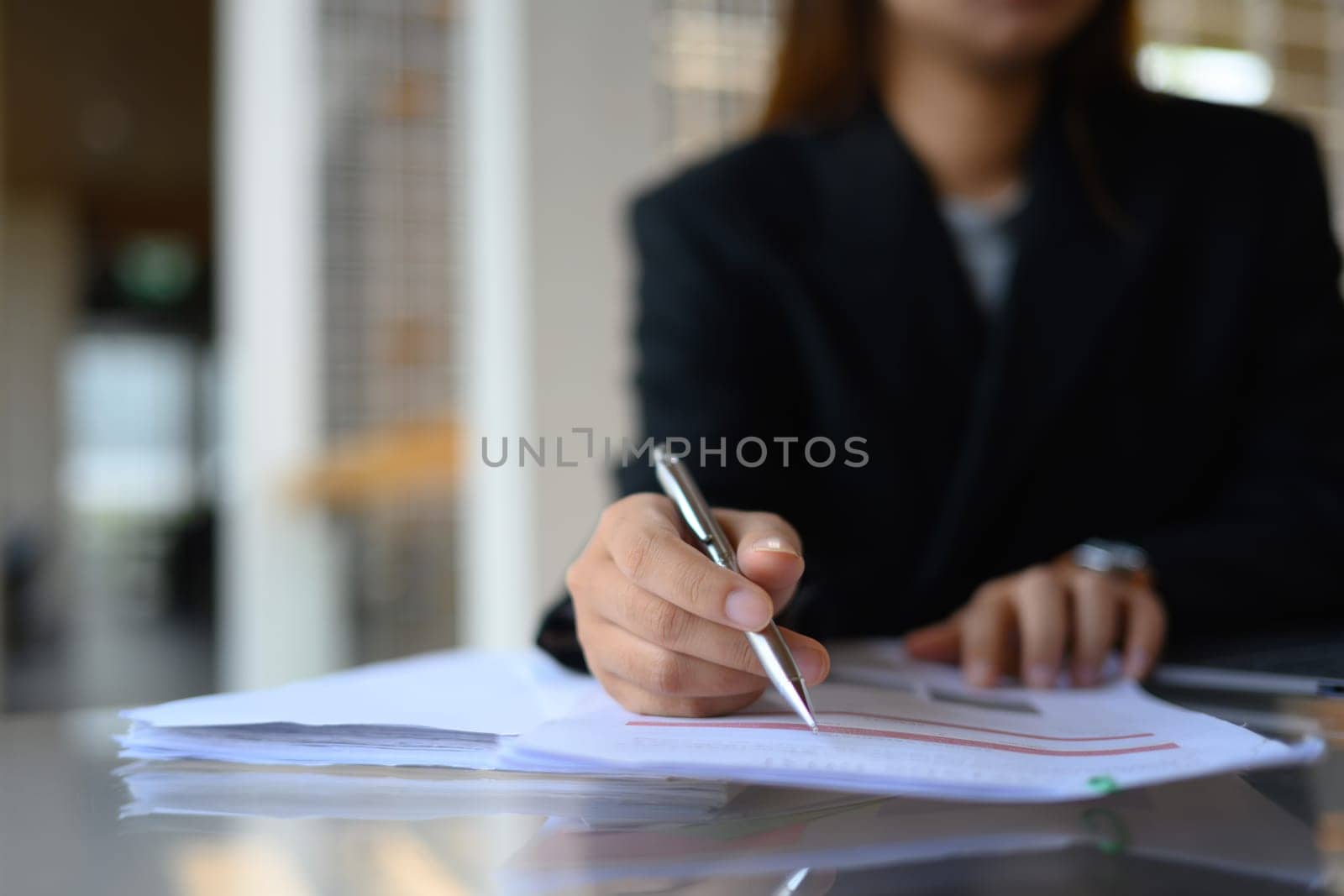 Focused on businesswoman hand writing on paper, filling paper business document at office desk.