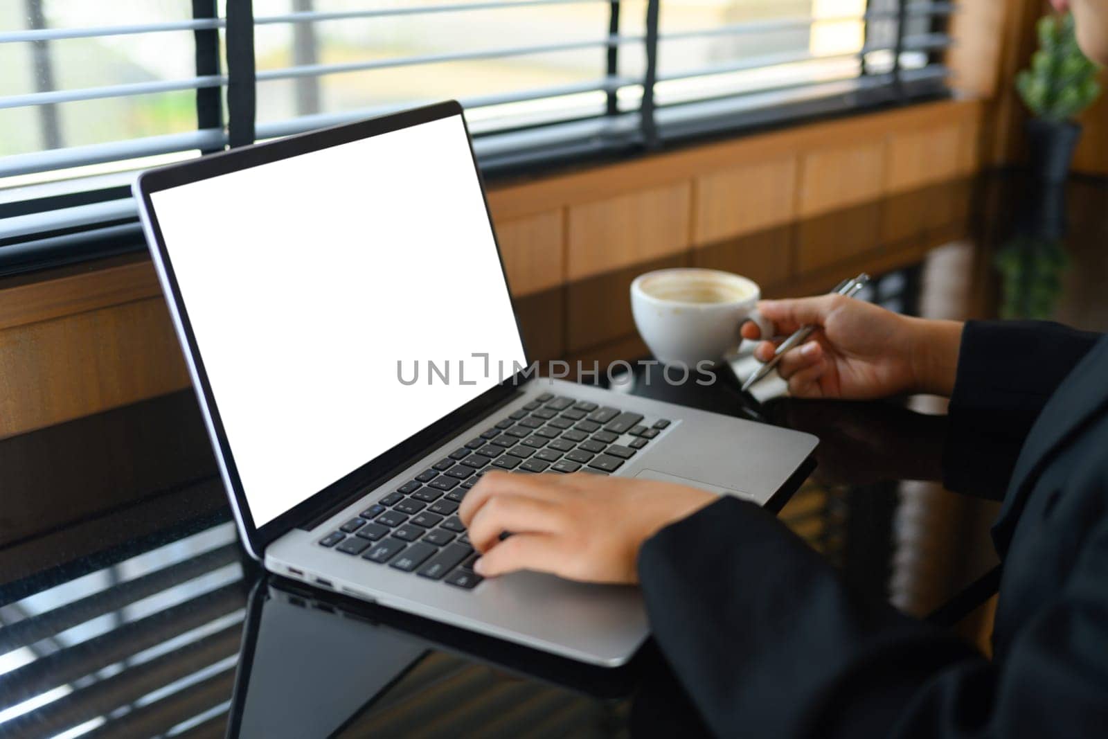 Female freelancer working and typing on laptop keyboard while sitting at modern coffee shop.