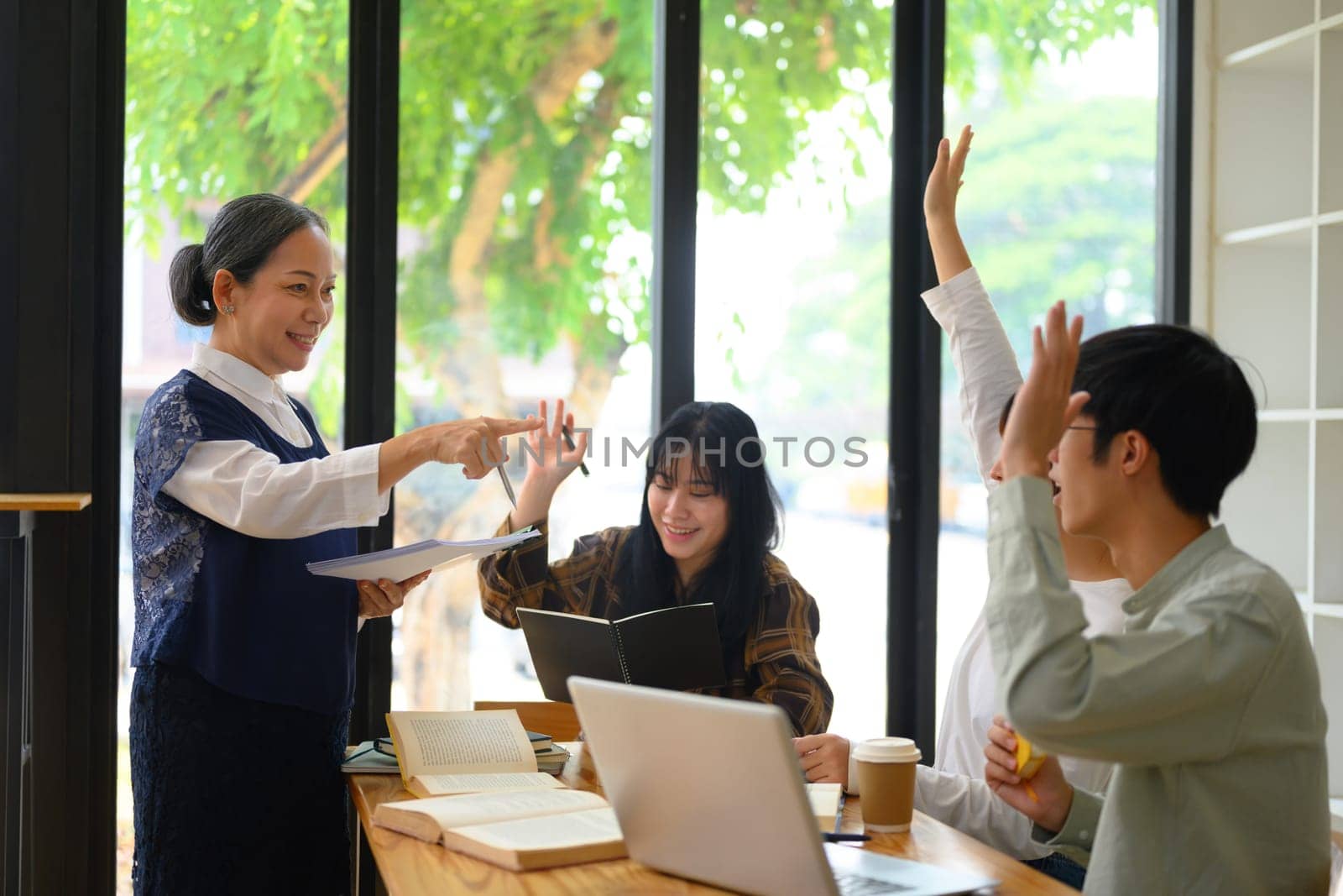 Active college students raising hands to answer teacher's question during class by prathanchorruangsak