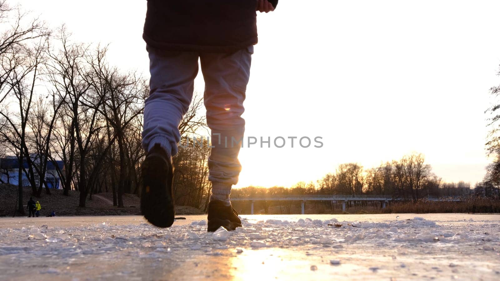 The lonely figure of a man walking on the frozen river at sunset, with peace of crystals ice in forward line , the reflection of the sun on the ice