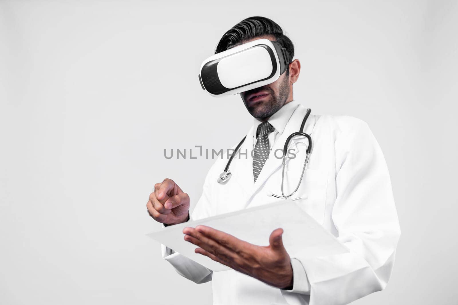 Doctor wearing virtual reality glasses while looking medical chart at white background. Professional doctor with lab coat using VR glasses while holding and pointing at application form. Deviation.