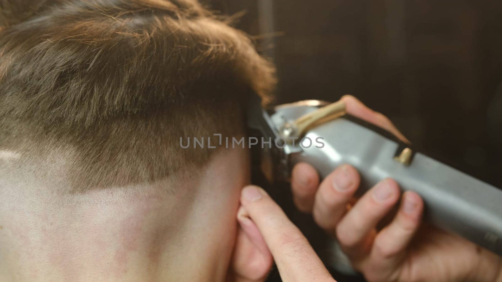 close up men's hairstyling and haircutting with hair clipper in a barber shop or hair salon. Hairdresser service in a modern barbershop in a dark key lightning with warm light and smoke back view.