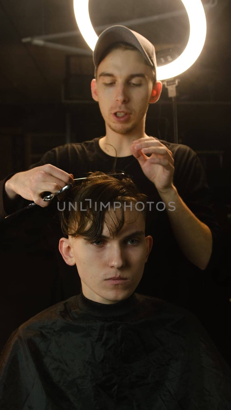 Barber master hairdresser does hairstyle and style with scissors and comb. Concept Barbershop. front view in dark key lightning with warm light.