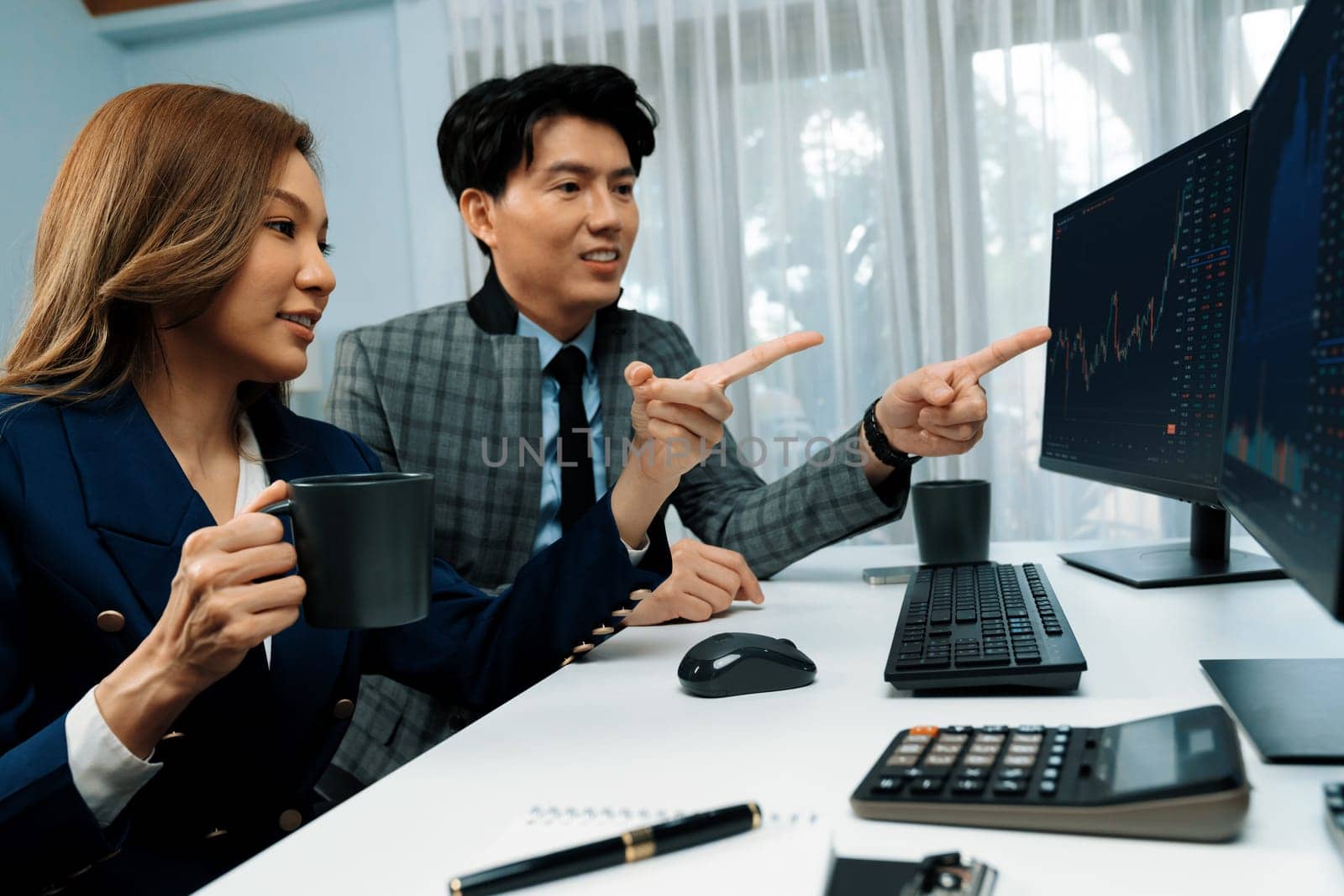 Successful of smiling Asian businesswoman holding cup while pointing to dynamic stock exchange data screen with businessman partner of profit value online website program at home office. Infobahn.
