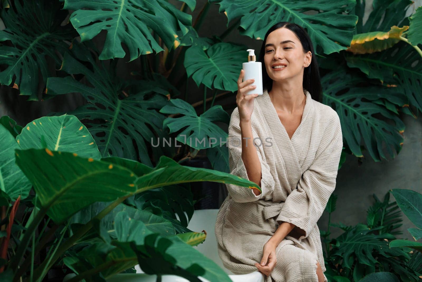 Tropical and exotic spa garden with bathtub in modern hotel or resort with woman in bathrobe holding beauty skincare product while enjoying leisure lush with greenery foliage background. Blithe