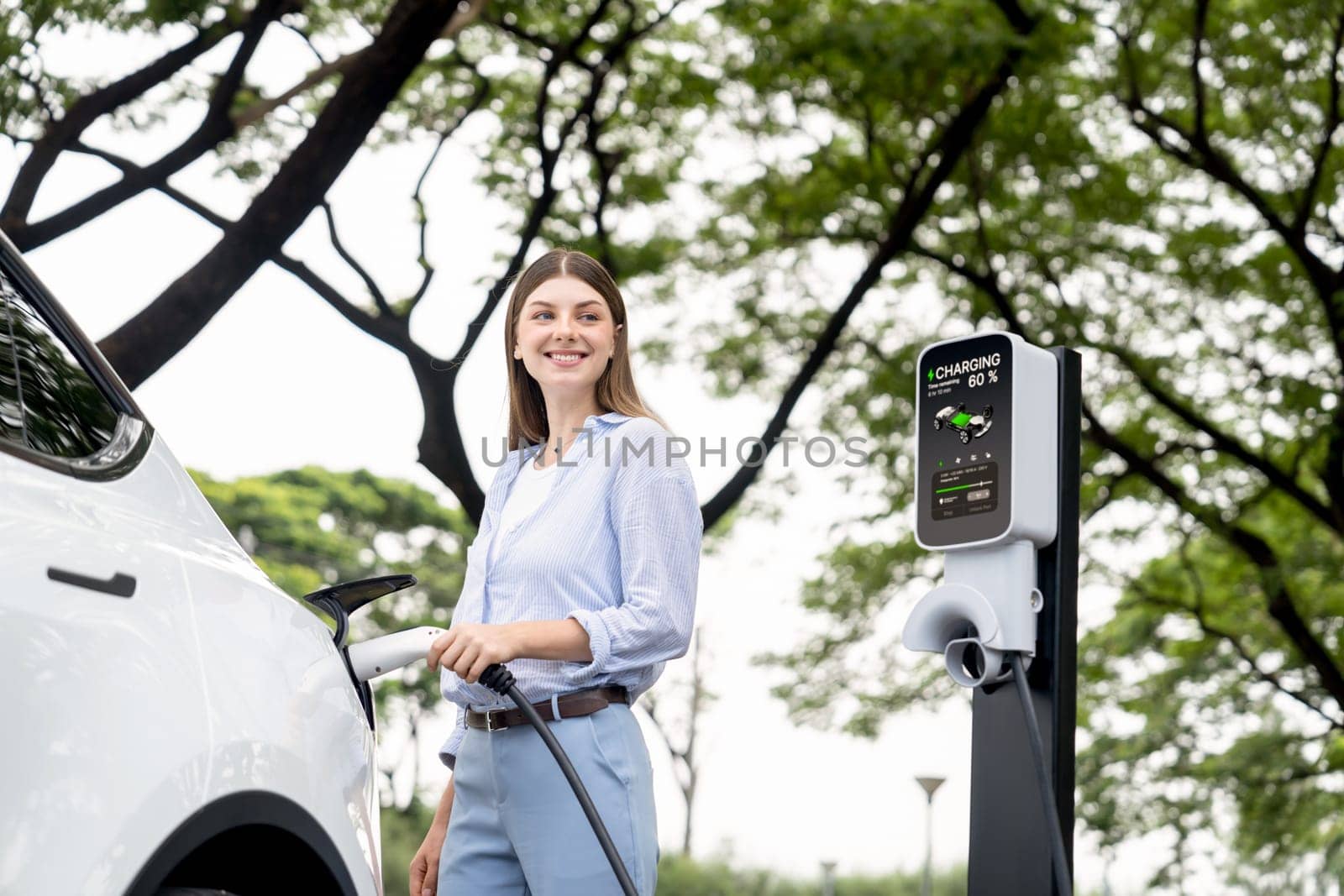 Young woman recharging battery for electric car during road trip. Exalt by biancoblue