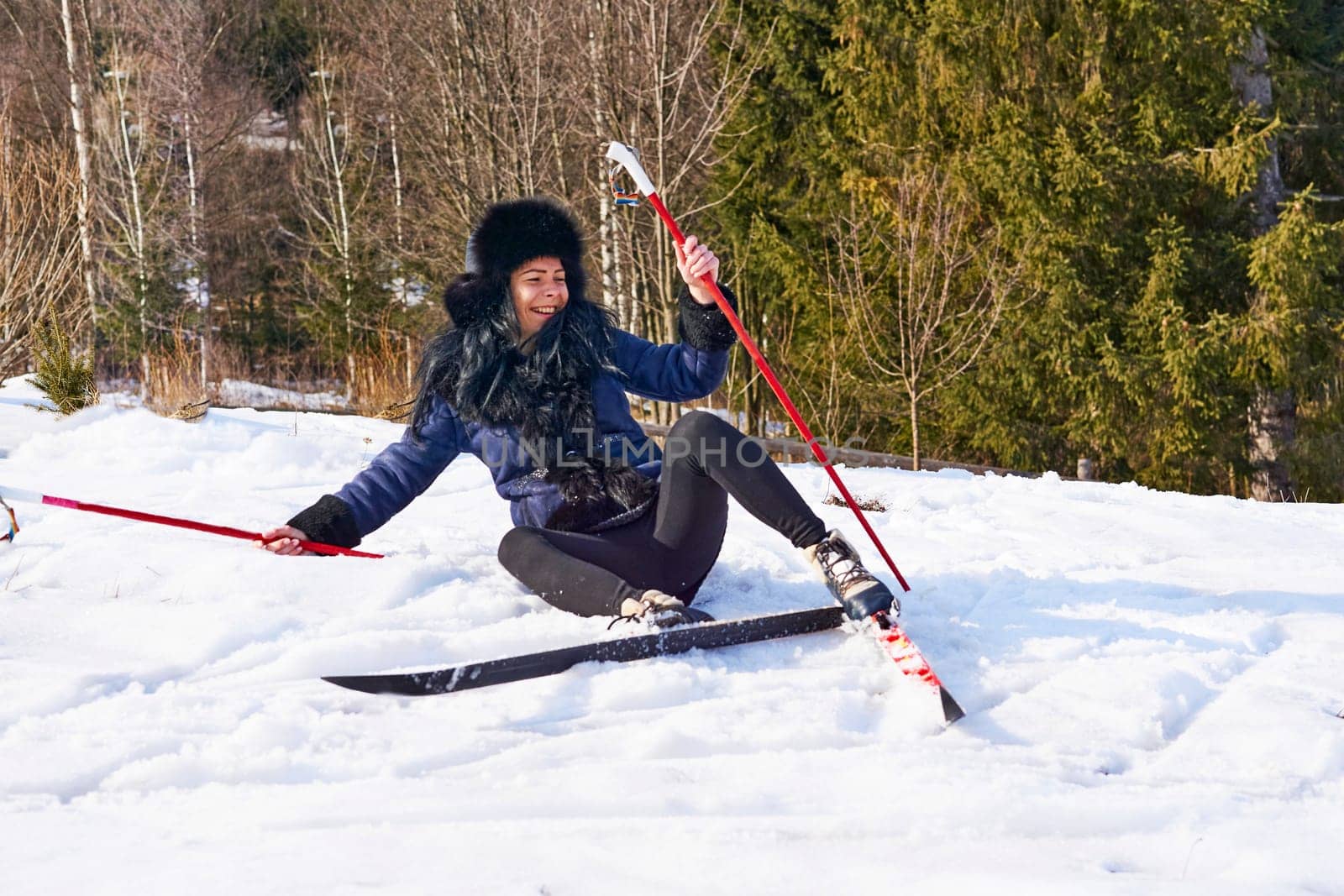 the action of traveling over snow on skis, especially as a sport or recreation. Laughing cheerful young girl fell down while skiing in the forest.