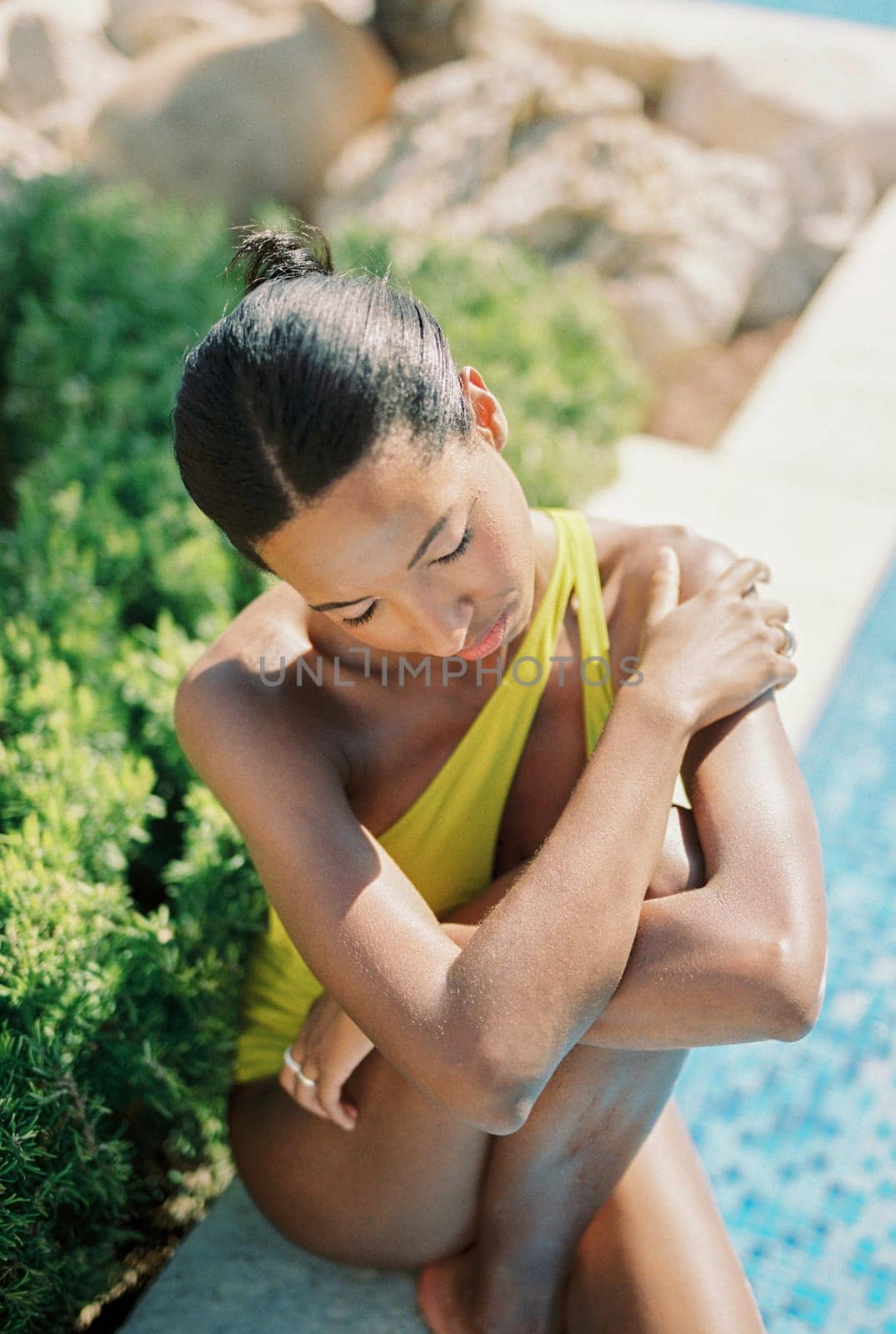 Young woman sitting with eyes closed on the edge of the pool, hugging her knee. High quality photo