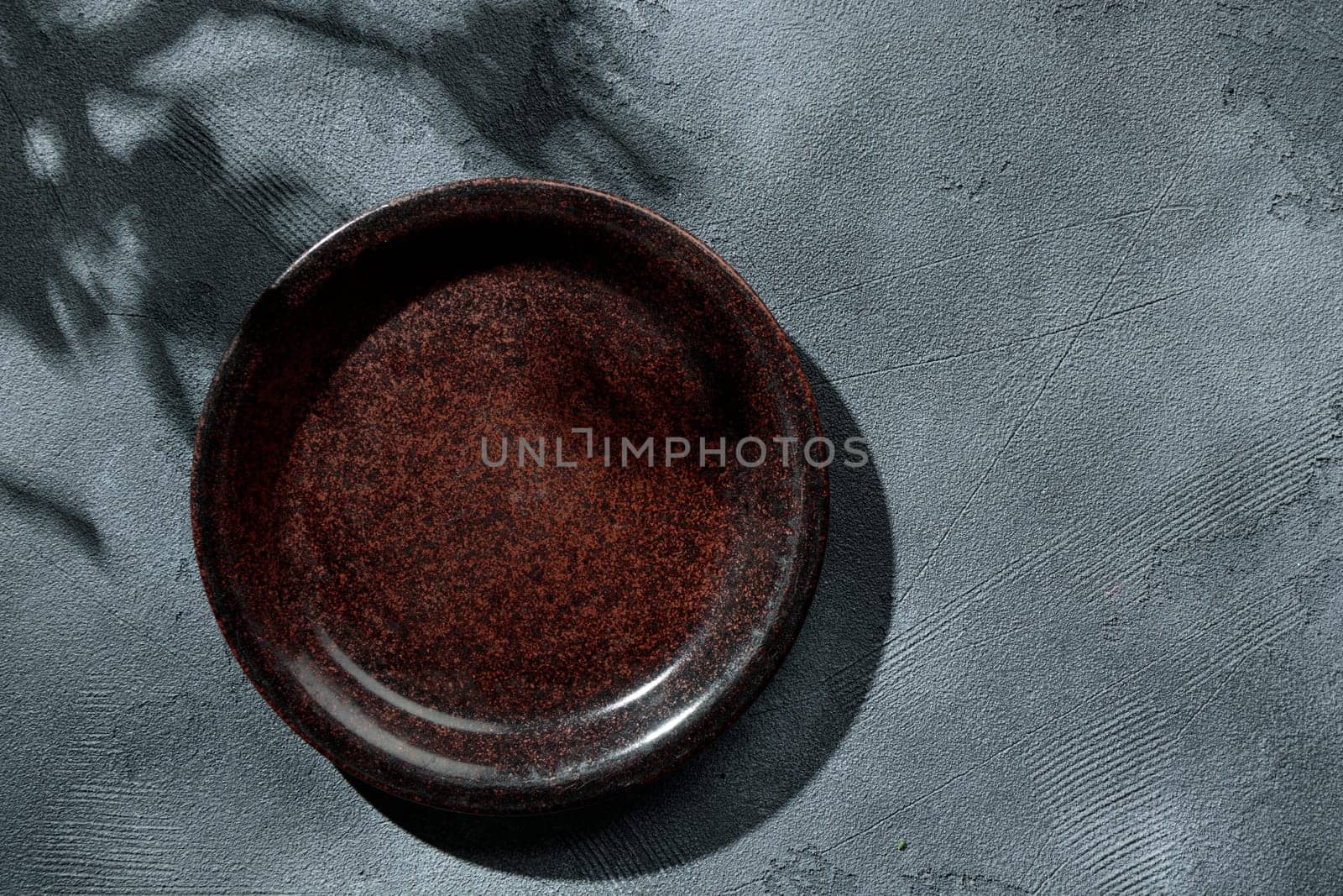 Brown rustic empty plate on stone table top view, sunny day, shadows, summer. Table setting mock up. Vertical