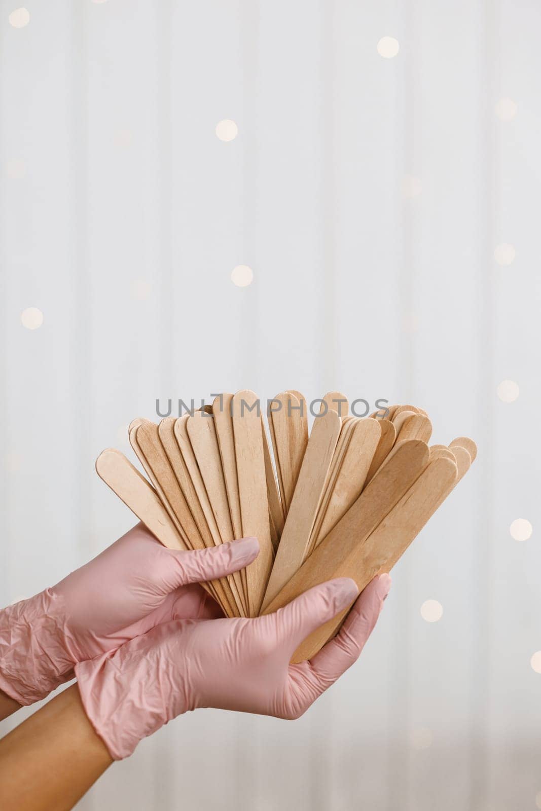 Woman holding many wax wooden spatulas. The young woman is wearing beige clothing and in pink medical gloves. The concept of depilation, waxing, sugaring smooth skin without hair, banner, copy space