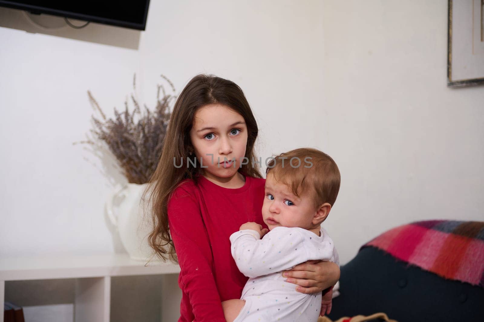 Caucasian cute child girl hugging her little baby brother at home. The concept of family relationships and care. International Children Day. Brother and sister together by artgf
