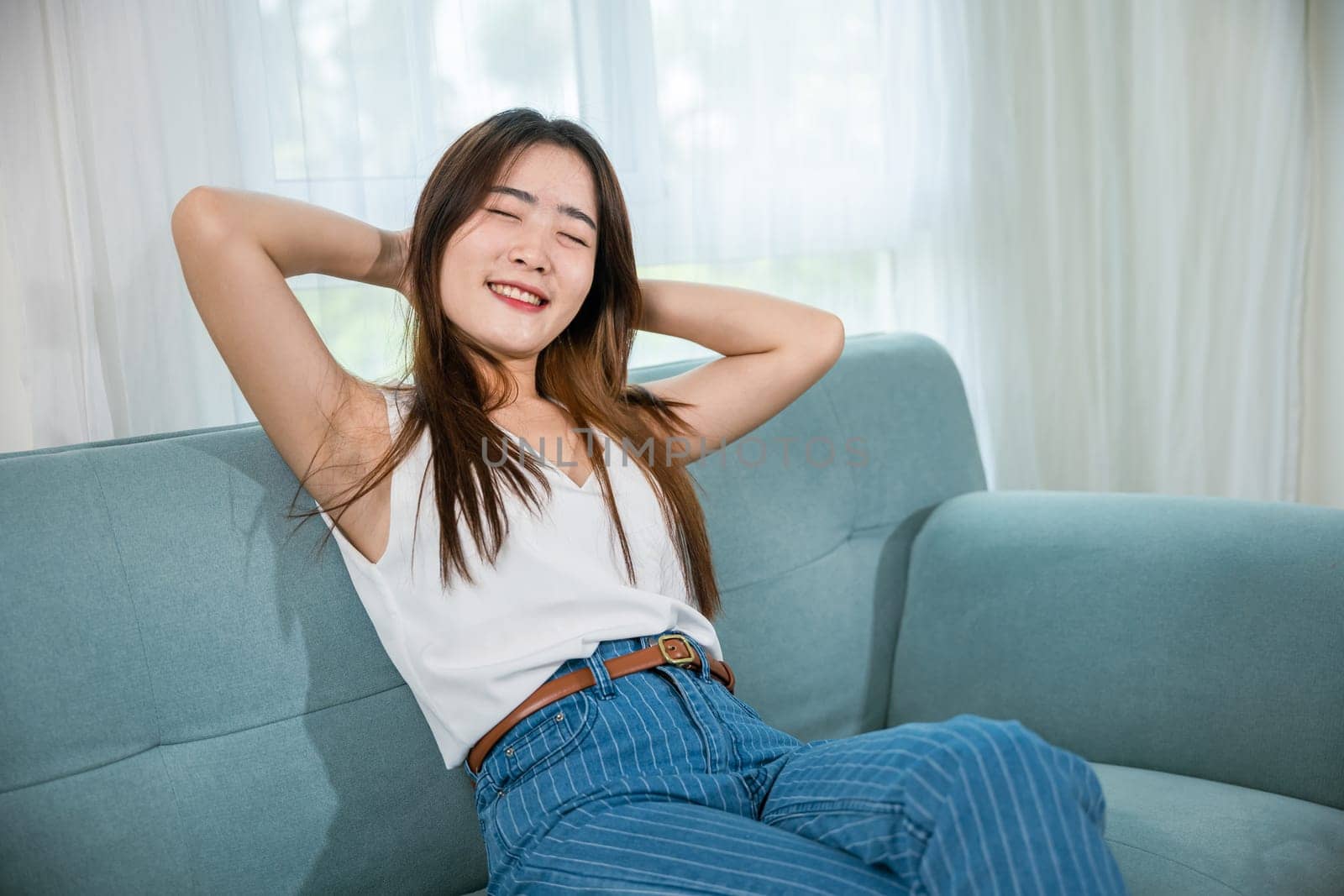 Happy woman feeling relax comfortable enjoying after homework, Asian young female enjoying free time relaxing put arm hand back behind head sitting on sofa in living room at home