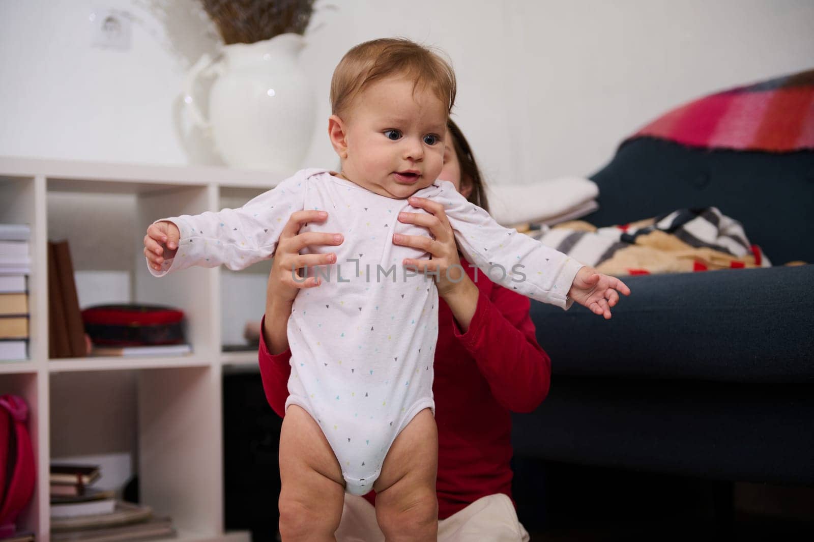 Adorable baby boy in white bodysuit, in his loving caring sister's hands playing with him at home. People. Childhood. Infancy. Babyhood. Kids education nd development. The concept of happy family