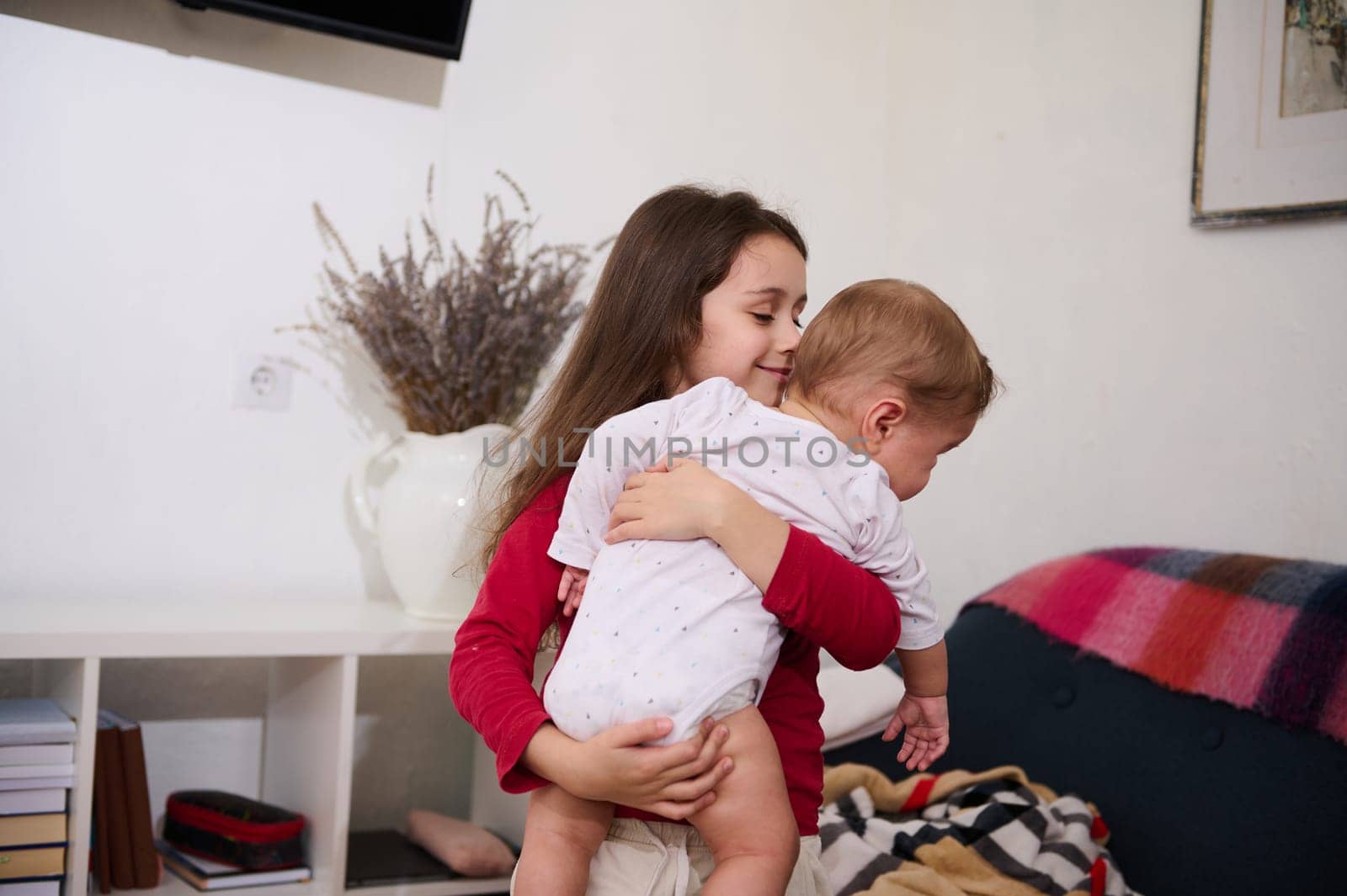 Beautiful girl 6 years old, smiles holding and hugging her little brother, cute baby boy of 6 months old. Family relationships concept. Love. Care. Tenderness. Affection. International Children's Day