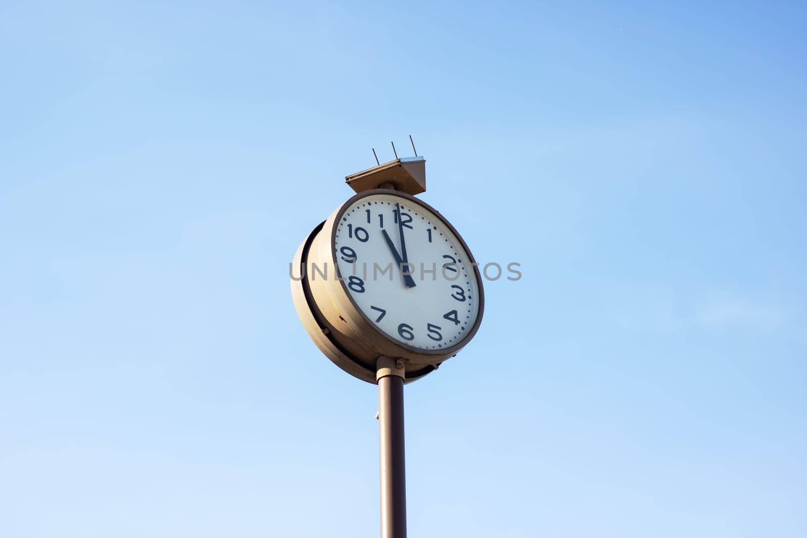 A quartz clock mounted on a metal pole displays the time as 1155 against a vibrant blue sky backdrop, adding a touch of elegance to the outdoor space