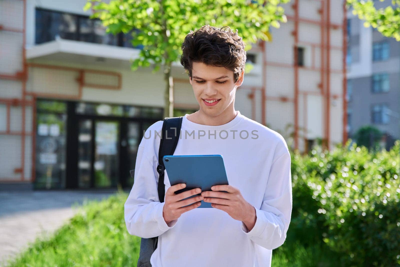 Young handsome guy college student using digital tablet outdoor, educational building background. Education, technology, training, 19,20 years age youth concept