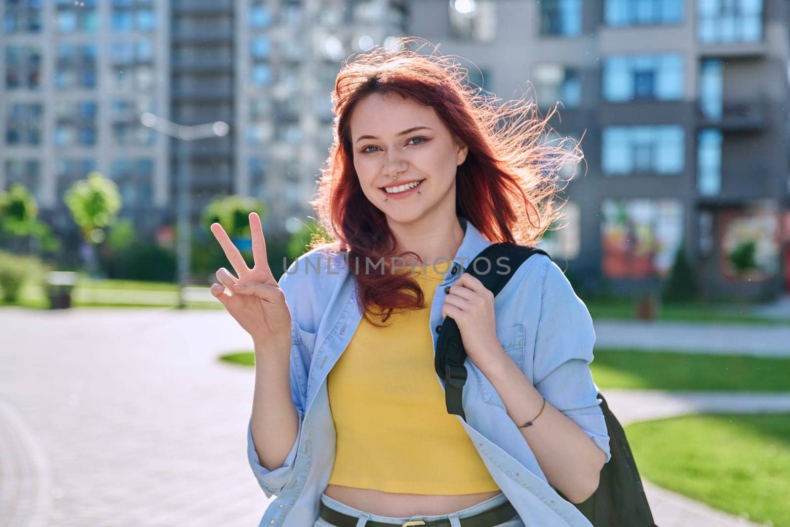 Young smiling red-haired hipster female with facial piercing looking at camera outdoor by VH-studio