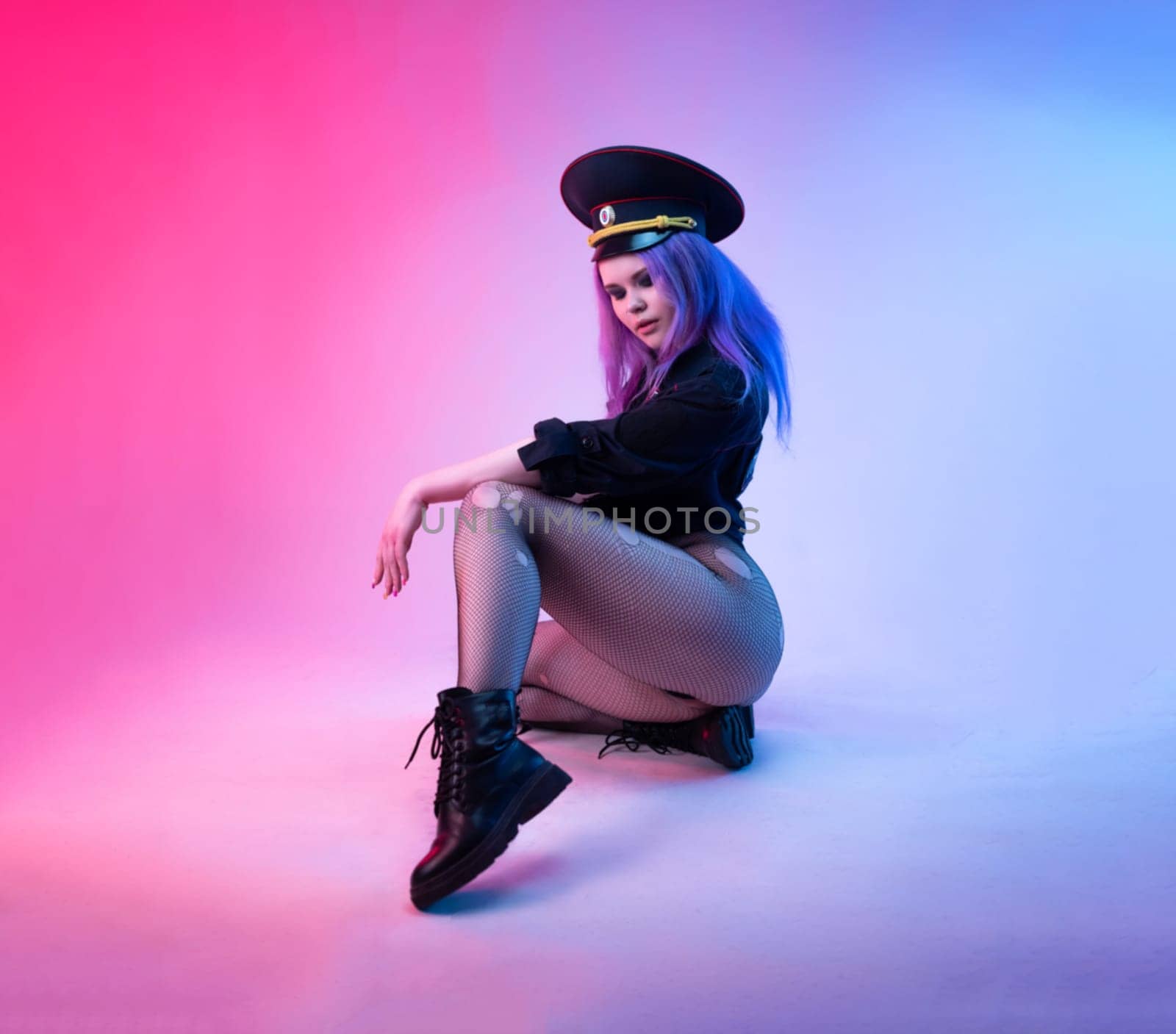 Sexy girl in police uniform posing in underwear with a police rubber baton in neon light on an empty background