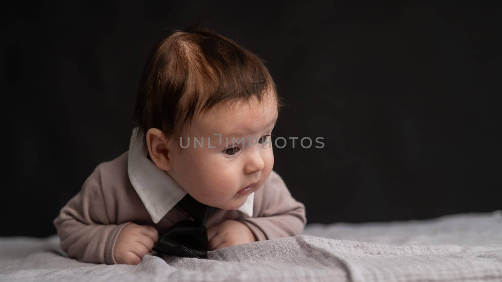 Portrait of a baby lying on his stomach wearing a tie on a black background. by mrwed54