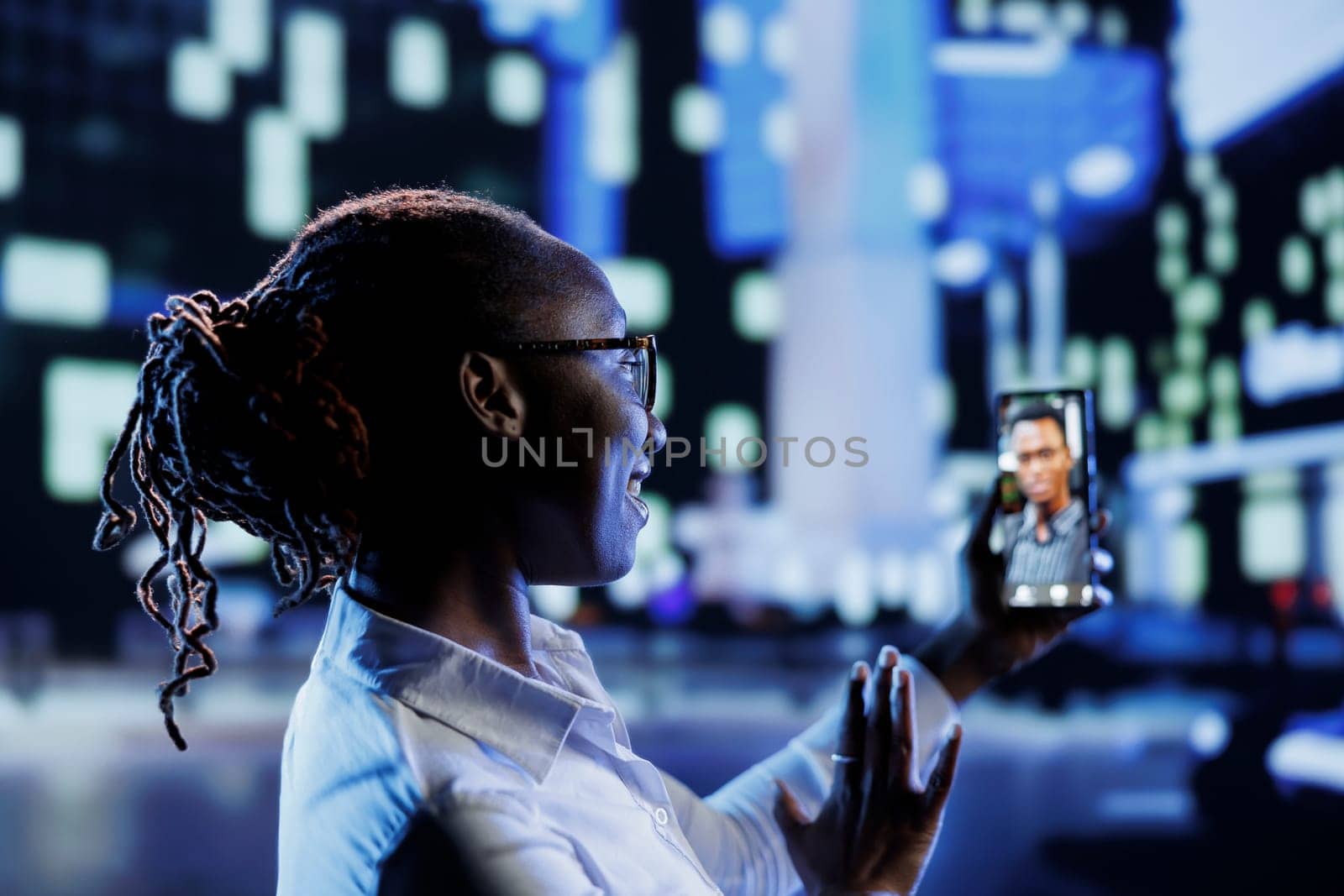 Woman in videocall with coworker while strolling around city streets at night, talking about her day at work. Citizen using smartphone to show workplace colleague surroundings in town center