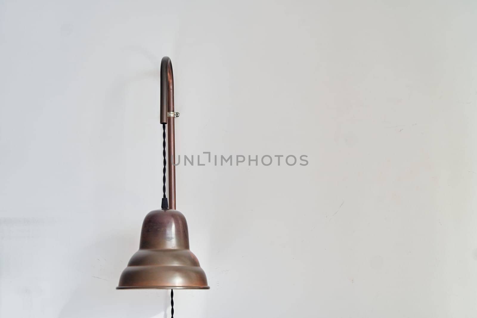 A bronze lamp with a steel finial is suspended from a wooden pole on a white wall, creating a striking still life composition