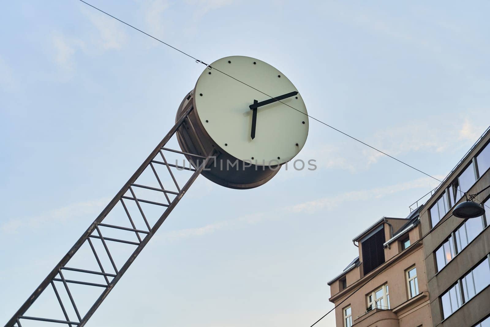 a large clock is hanging from a metal pole in front of a building by driver-s