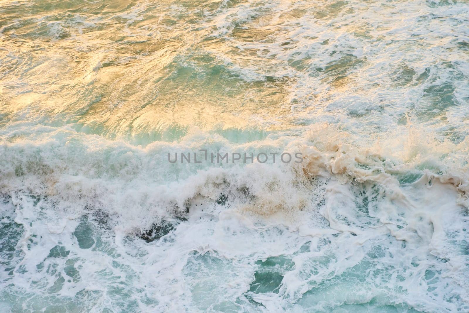 A closeup shot of the ocean with wind waves crashing onto the shore, creating a beautiful pattern of furrows in the water. The landscape is enhanced by cumulus clouds in the sky