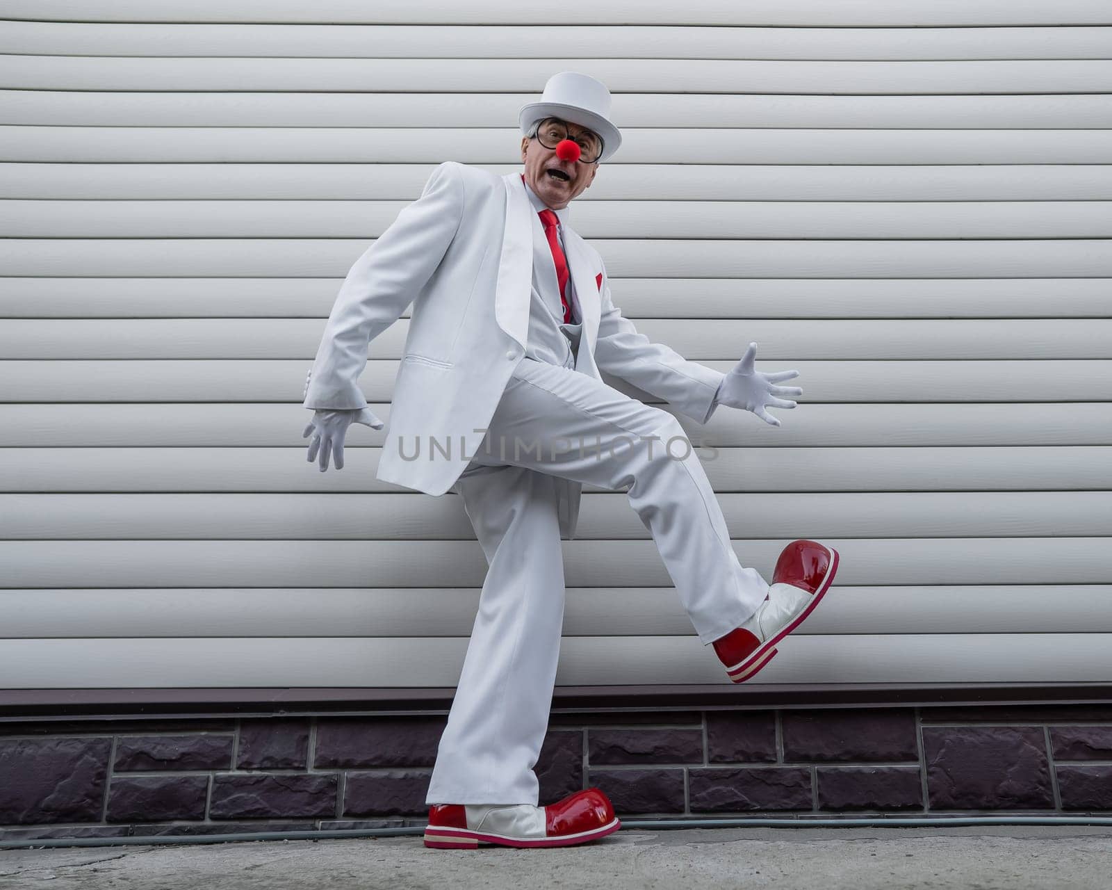 An elderly man in a white suit, huge boots and a clown nose walks funny. by mrwed54