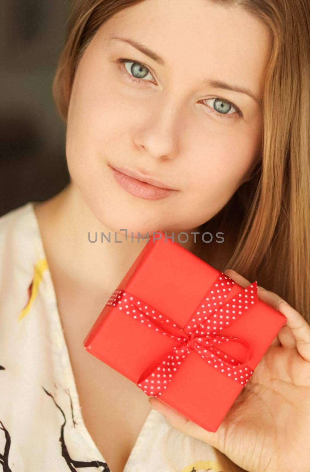 Happy smiling woman holding a red gift box, face portrait with natural make-up and holiday lifestyle at home by Anneleven