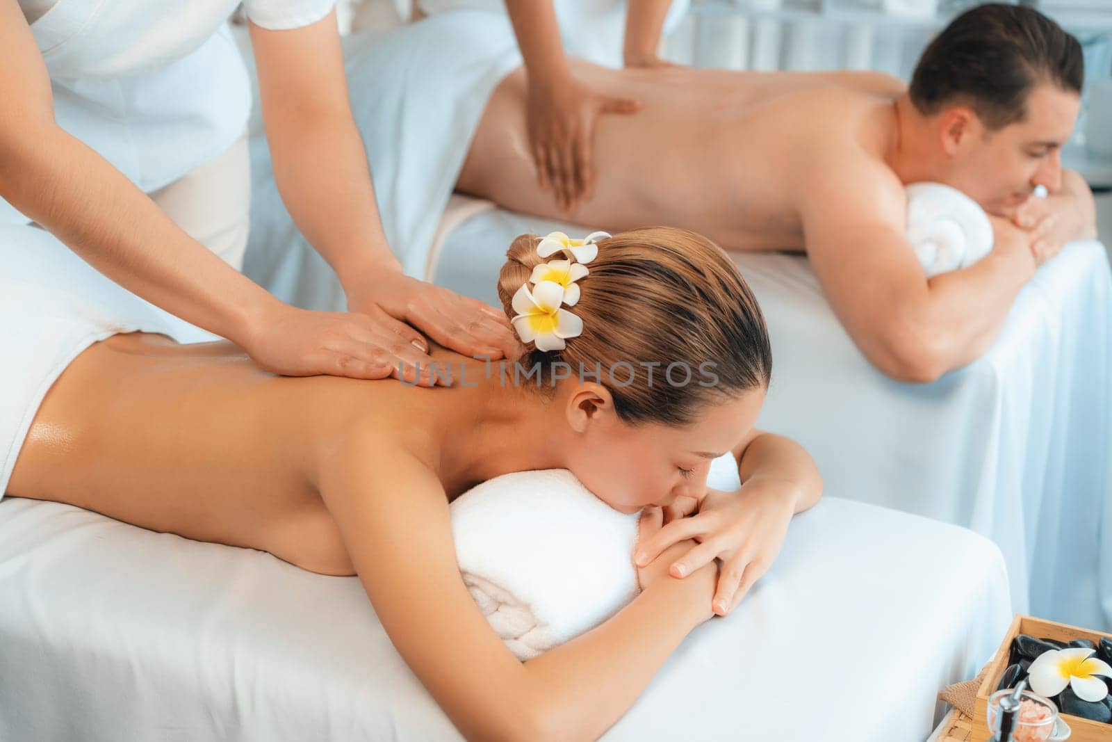 Caucasian couple customer enjoying relaxing anti-stress spa massage and pampering with beauty skin recreation leisure in day light ambient salon spa at luxury resort or hotel. Quiescent