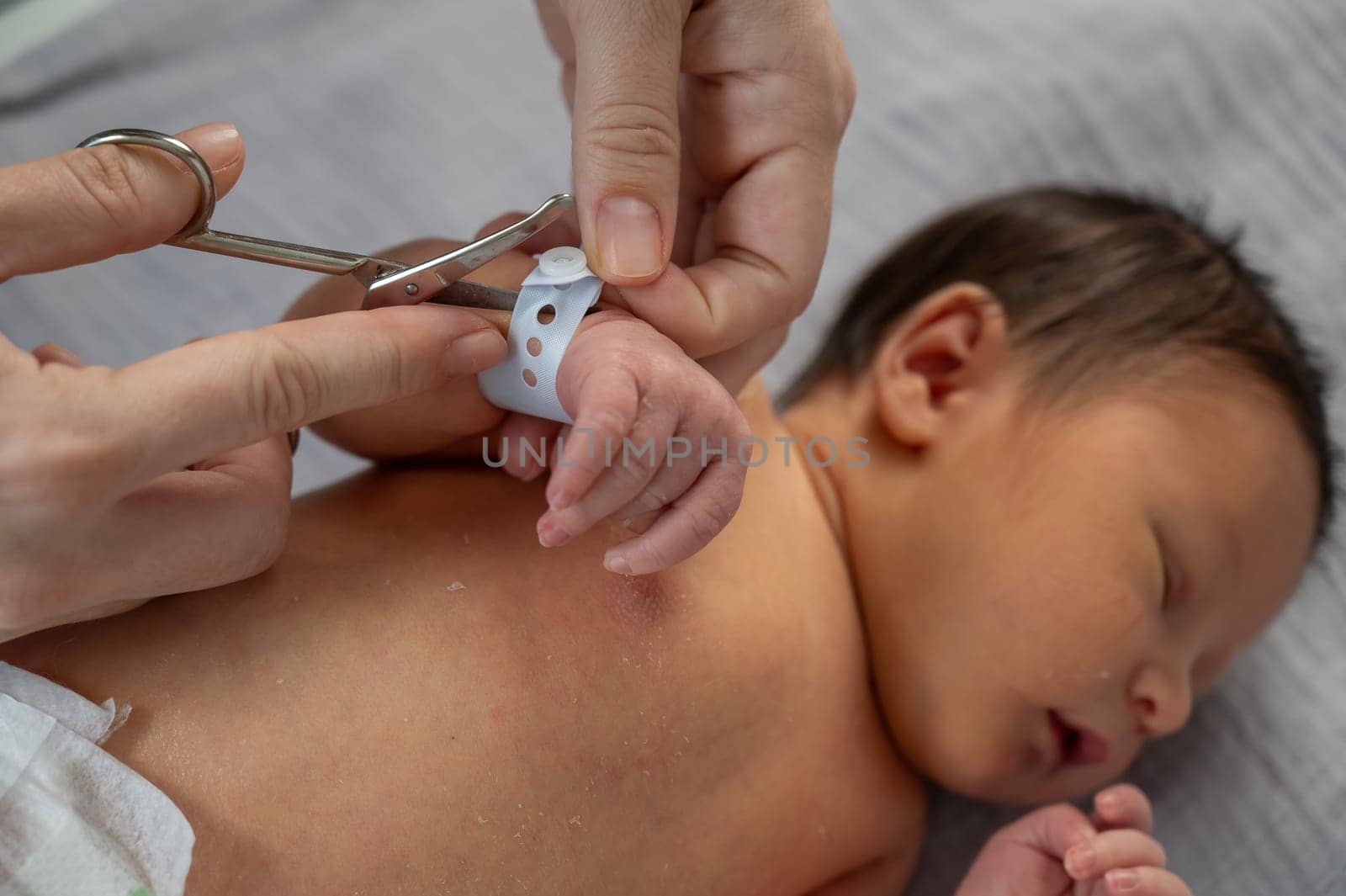 A woman cuts a tag from a newborn boy's hand with nail scissors. Close-up of hands. by mrwed54