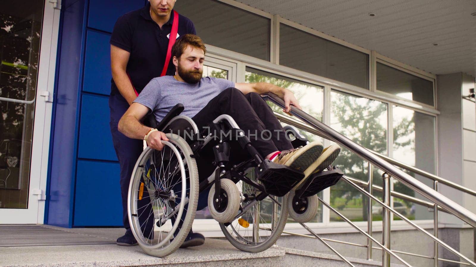A man helping to move down the stairs to a disabled person in a wheelchair