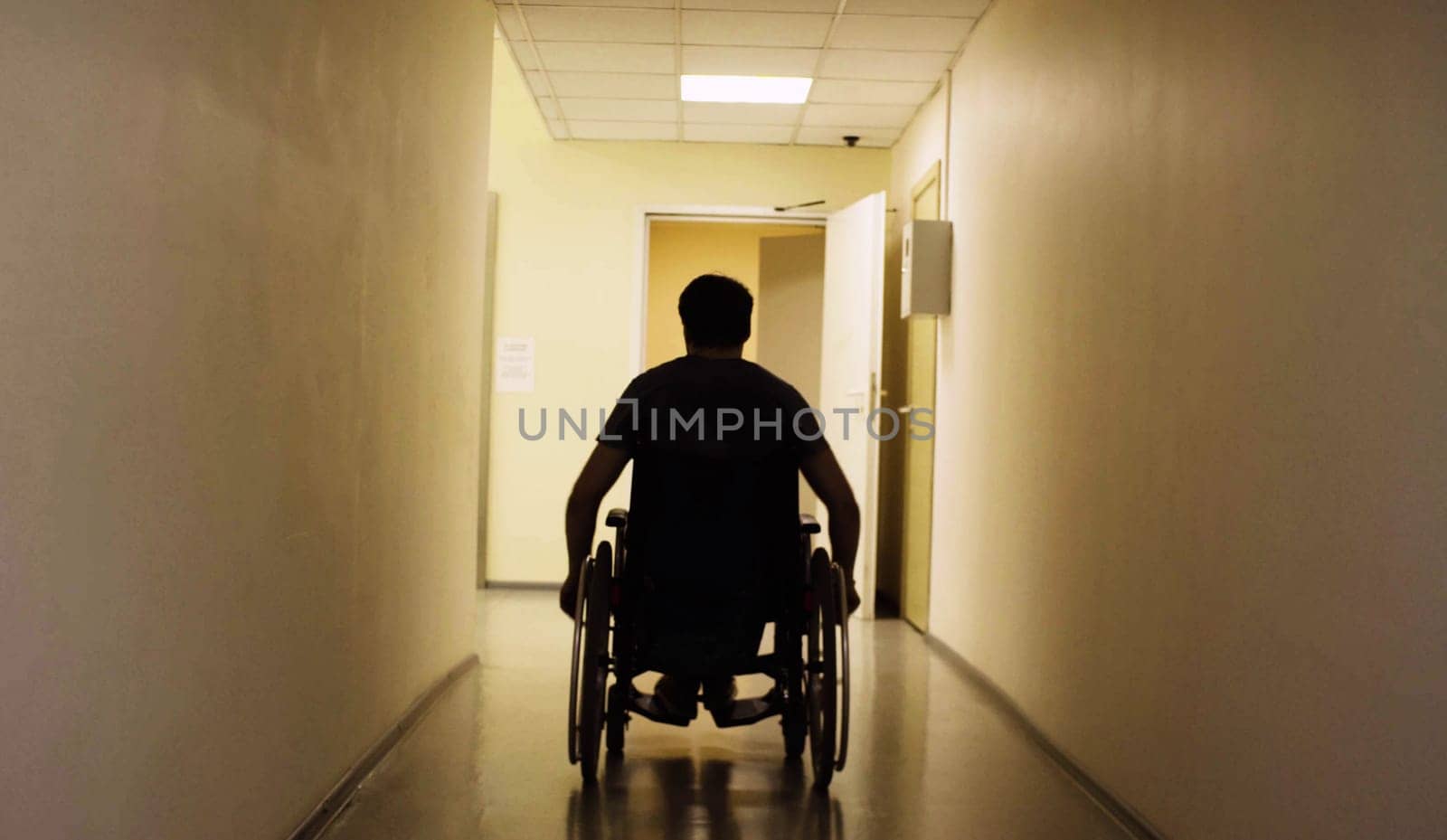 Silhouette of young disabled man in a wheelchair riding in the rehabilitation clinic. Rear view.