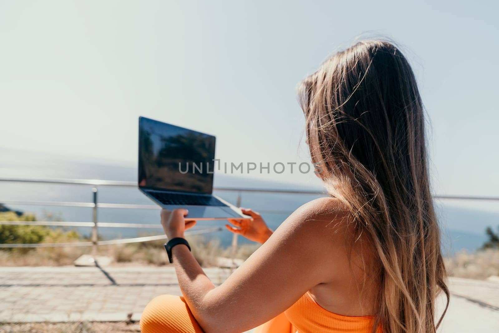 Digital nomad, Business woman working on laptop by the sea. Pretty lady typing on computer by the sea at sunset, makes a business transaction online from a distance. Freelance, remote work on vacation