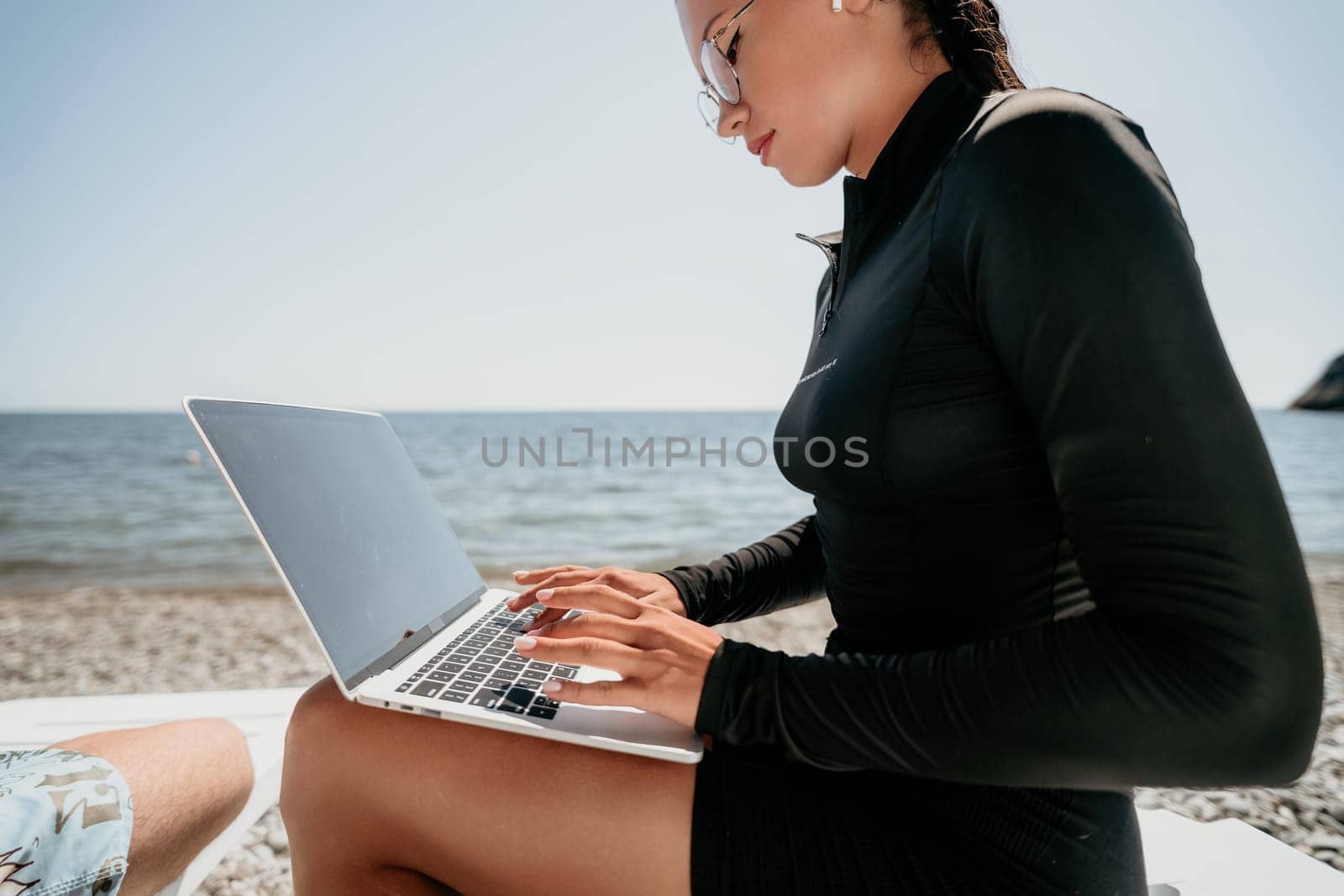 Digital nomad, Business man working on laptop by the sea. Man typing on computer by the sea at sunset, makes a business transaction online from a distance. Freelance, remote work on vacation