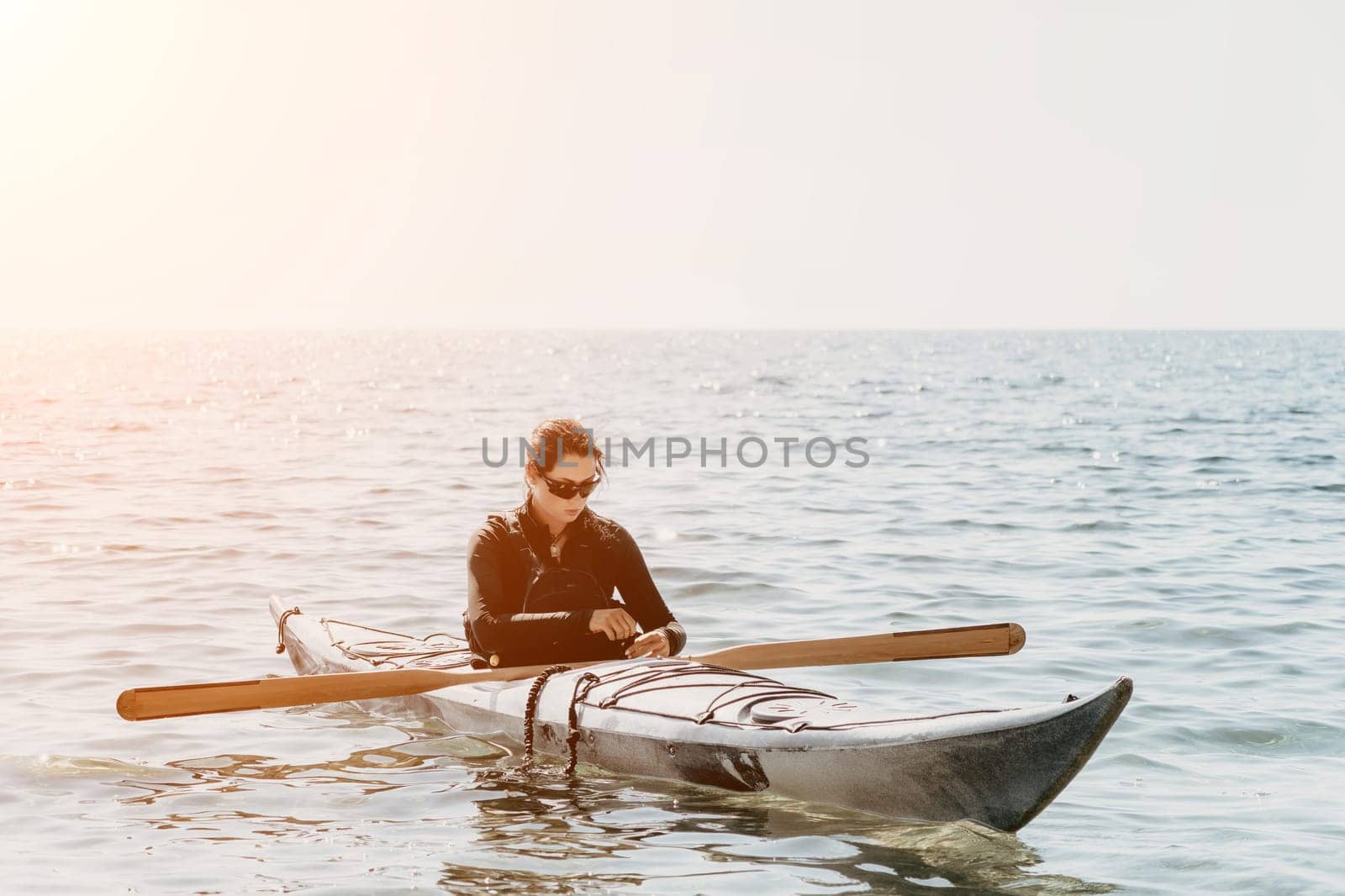 Happy smiling woman in kayak on ocean, paddling with wooden oar. Calm sea water and horizon in background