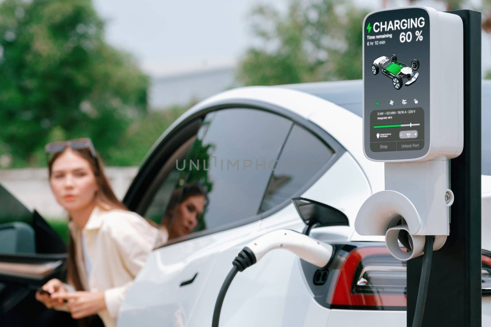 Young woman use smartphone to pay for electricity at public EV car charging station green city park. Modern environmental and sustainable urban lifestyle with EV vehicle. Expedient