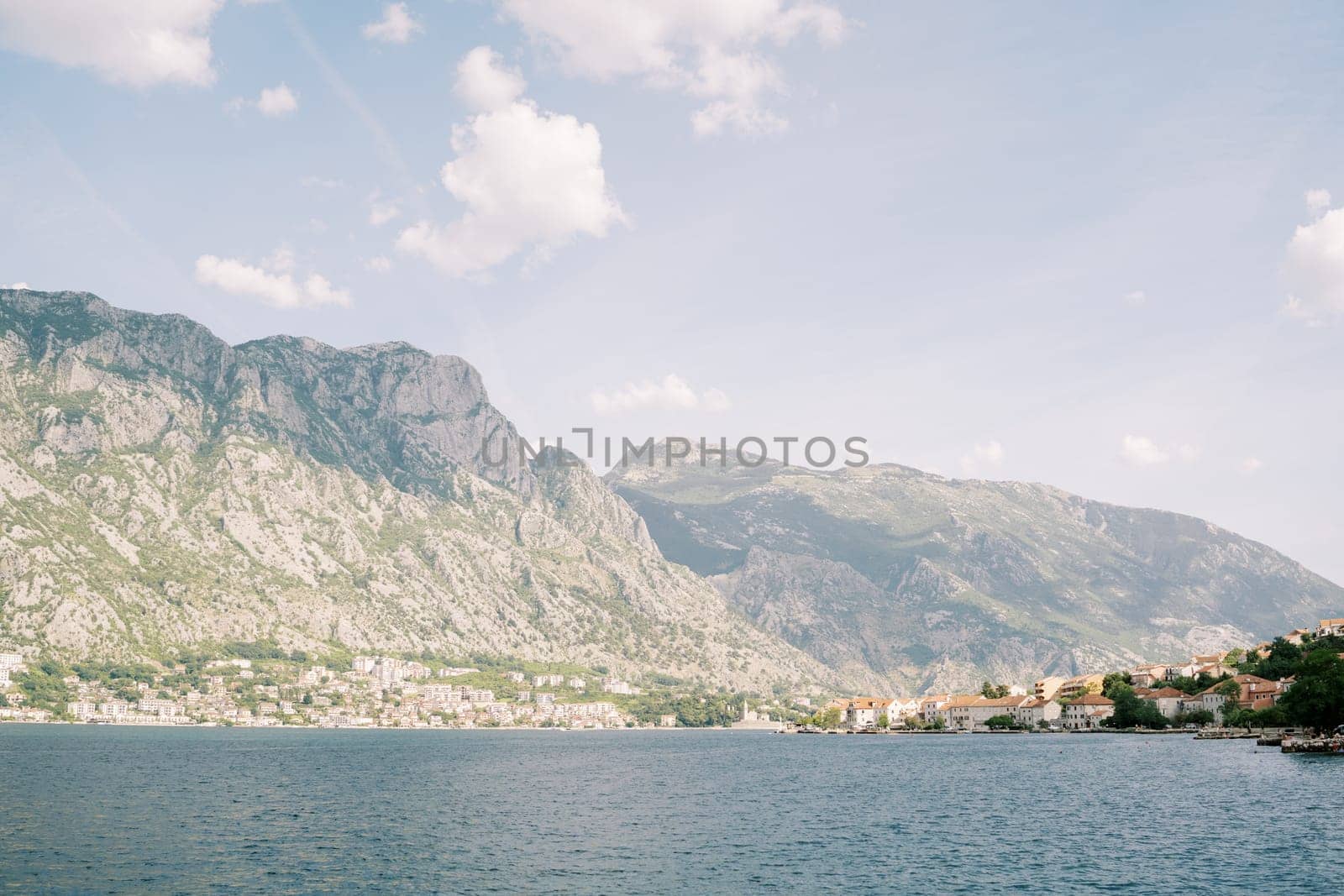 View from the sea to the coast of an ancient town with red roofs against the backdrop of a mountain range in a light haze. High quality photo