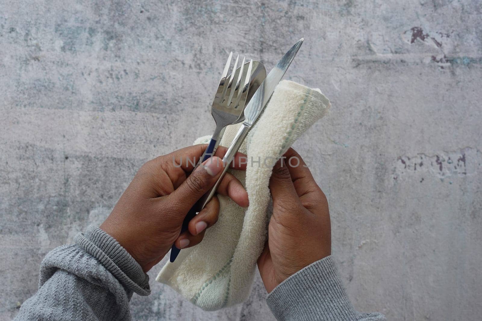 person hand cleaning and drying cutlery with a towel,