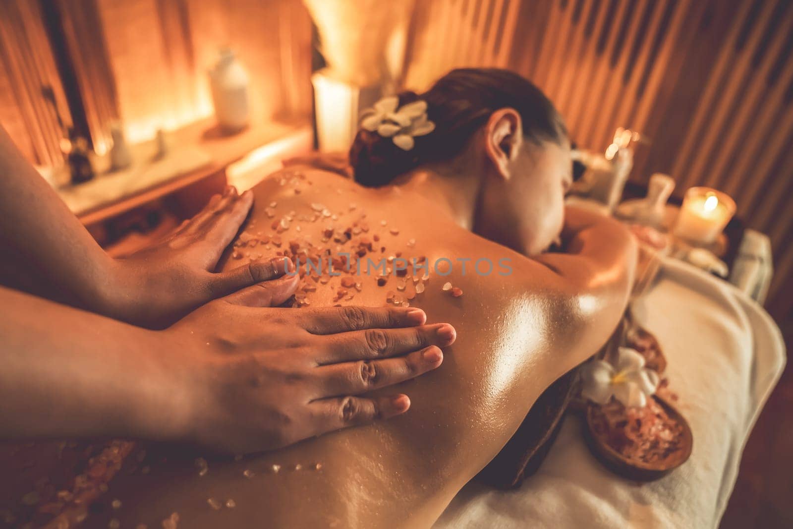 Woman customer having exfoliation treatment in luxury spa salon with warmth candle light ambient. Salt scrub beauty treatment in Health spa body scrub. Quiescent