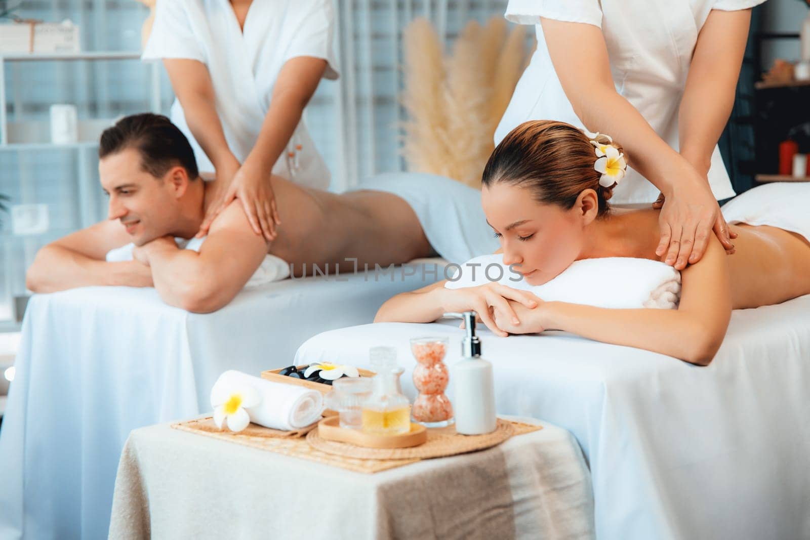 Caucasian couple customer enjoying relaxing anti-stress spa massage and pampering with beauty skin recreation leisure in day light ambient salon spa at luxury resort or hotel. Quiescent