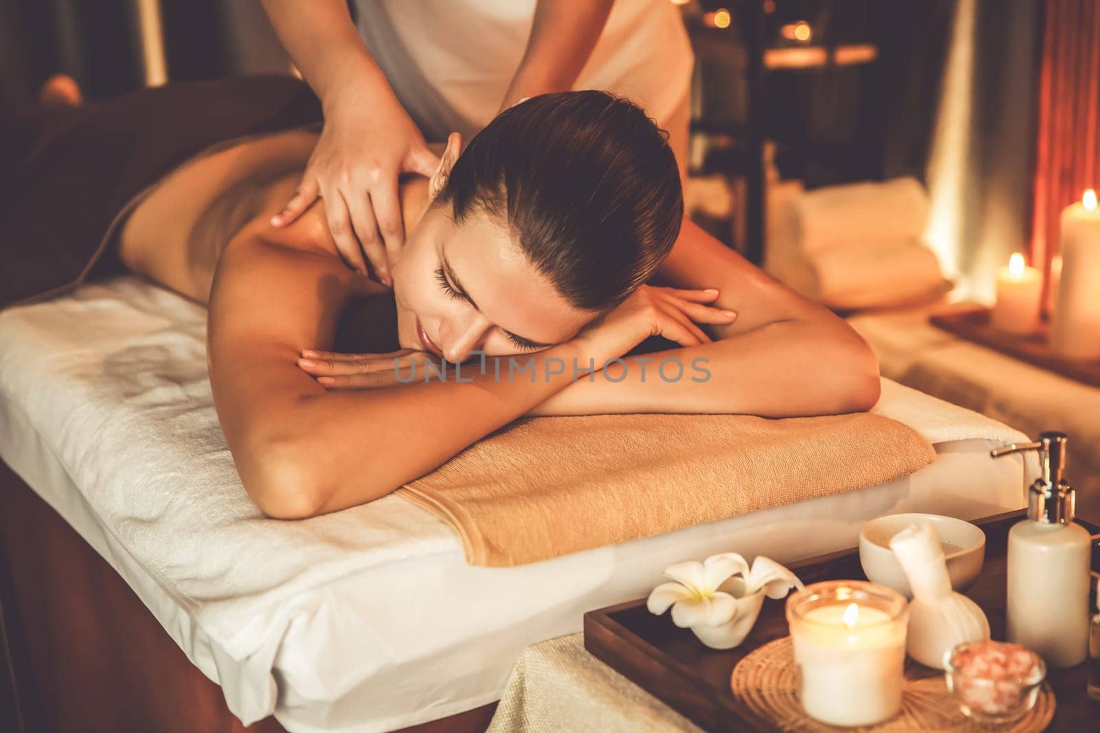 Caucasian woman customer enjoying relaxing anti-stress spa massage and pampering with beauty skin recreation leisure in warm candle lighting ambient salon spa at luxury resort or hotel. Quiescent