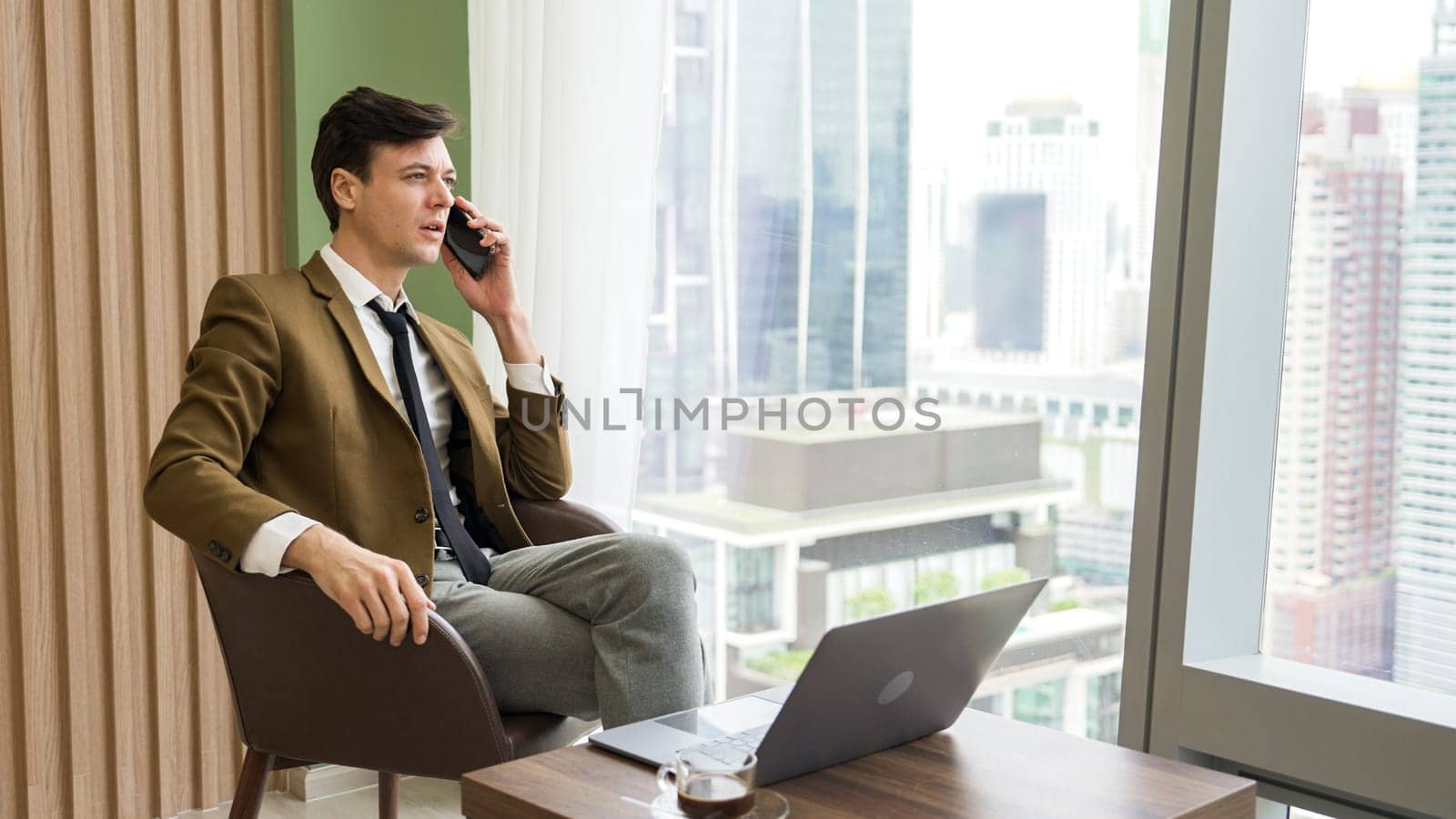 Businessman sitting on furniture working on laptop at ornamented corporate by biancoblue