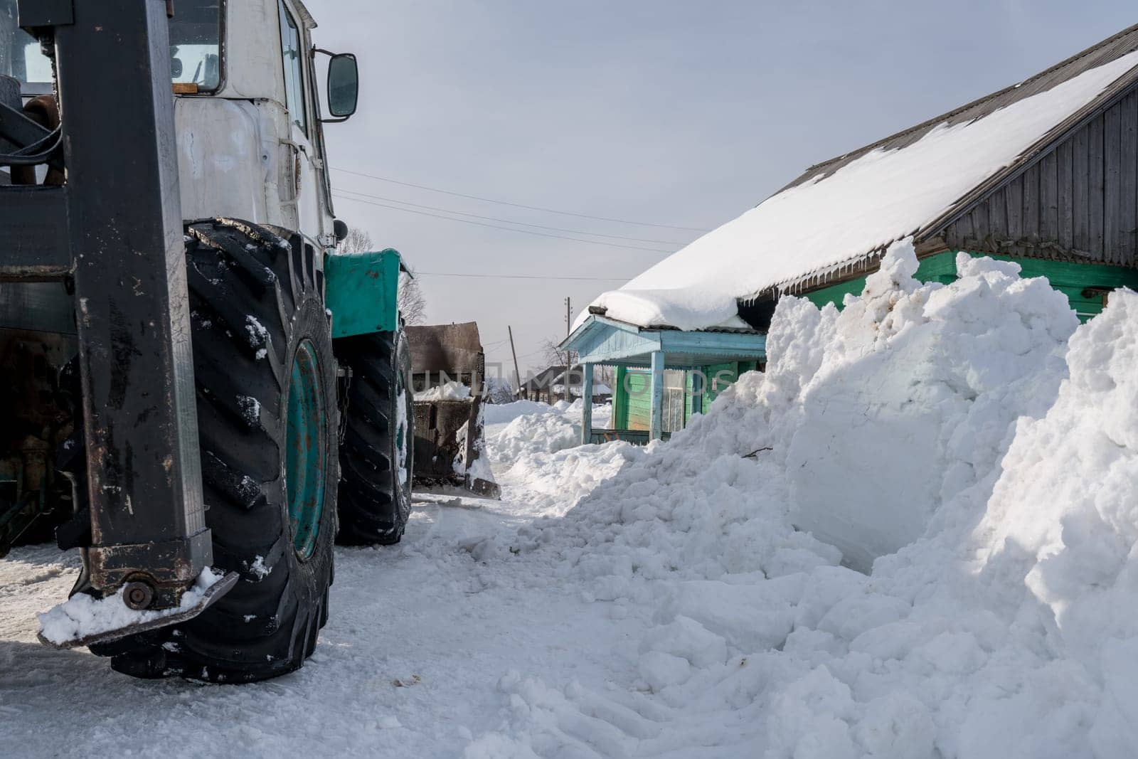 Winter time. Tractor cleans snow in village by rivertime