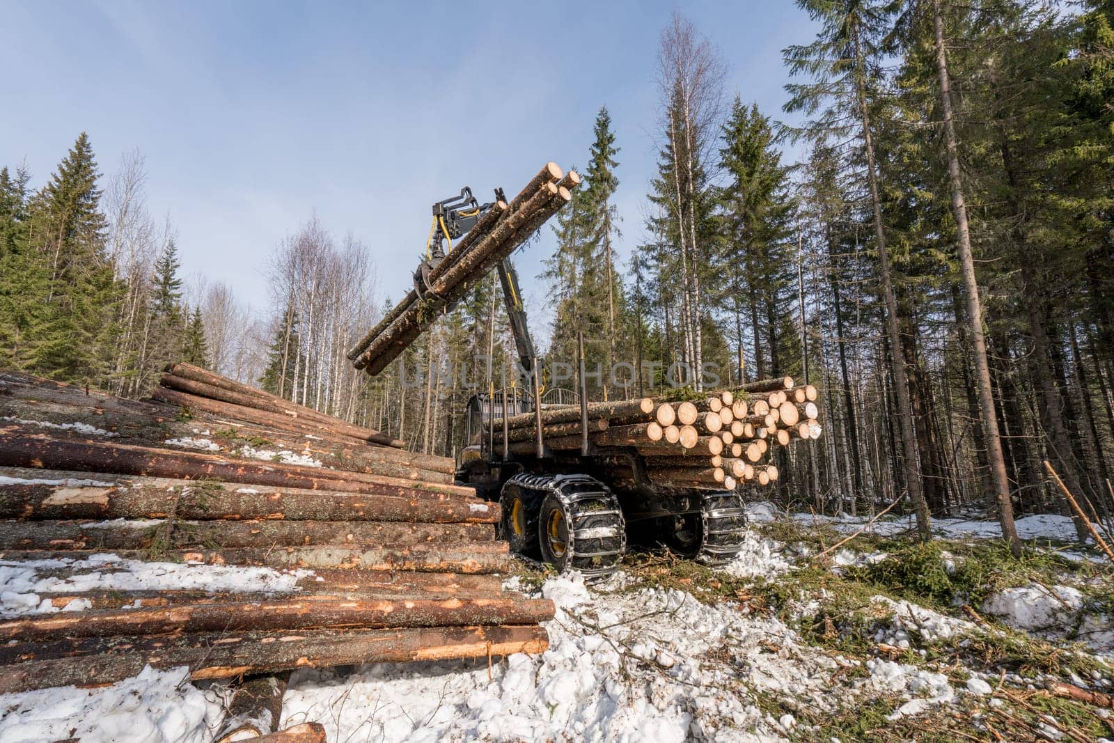 Image of machine with robotic arm lifts logs in winter forest