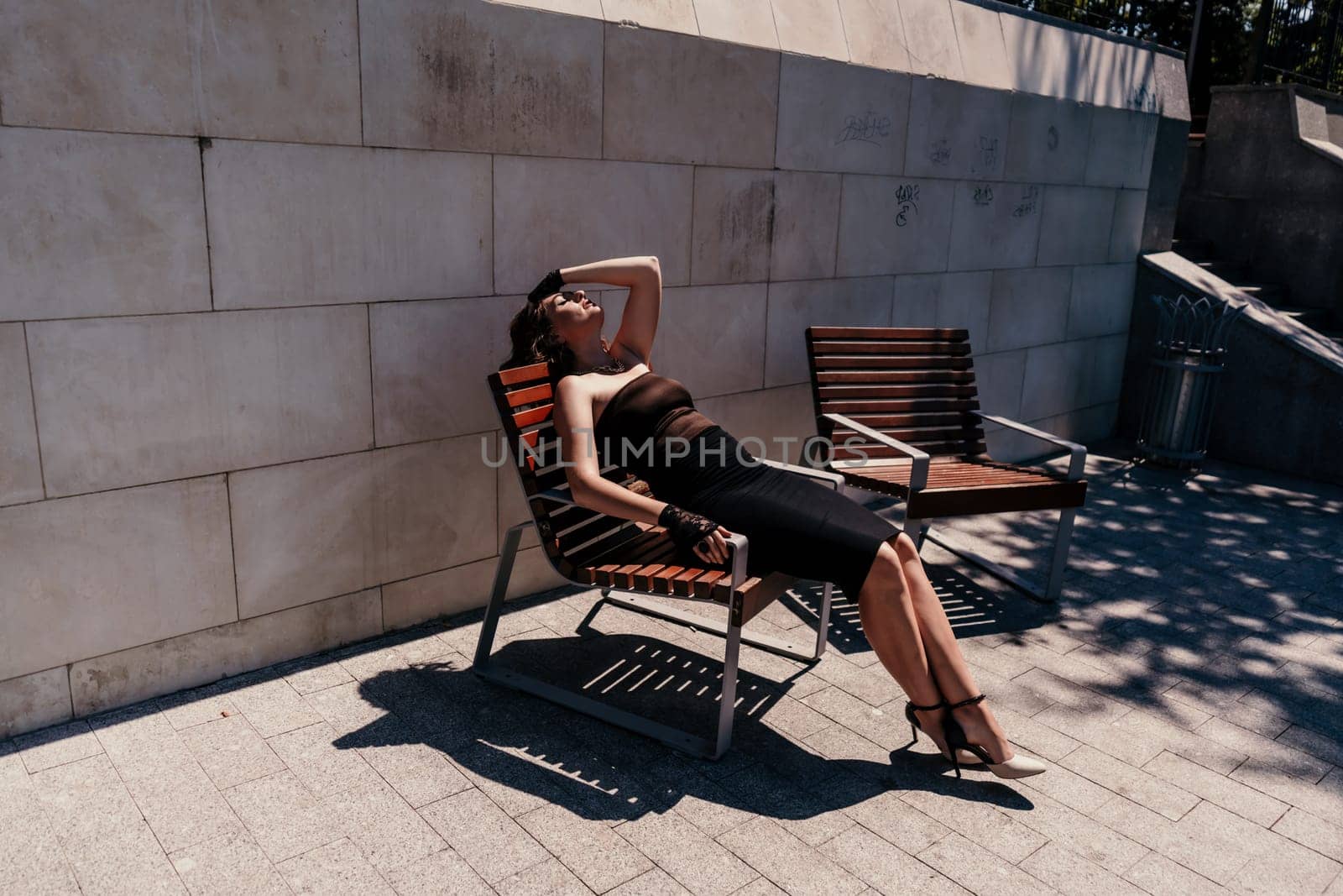 Portrait of a woman on the street. An attractive woman in a black dress is sitting on a bench outside. by Matiunina
