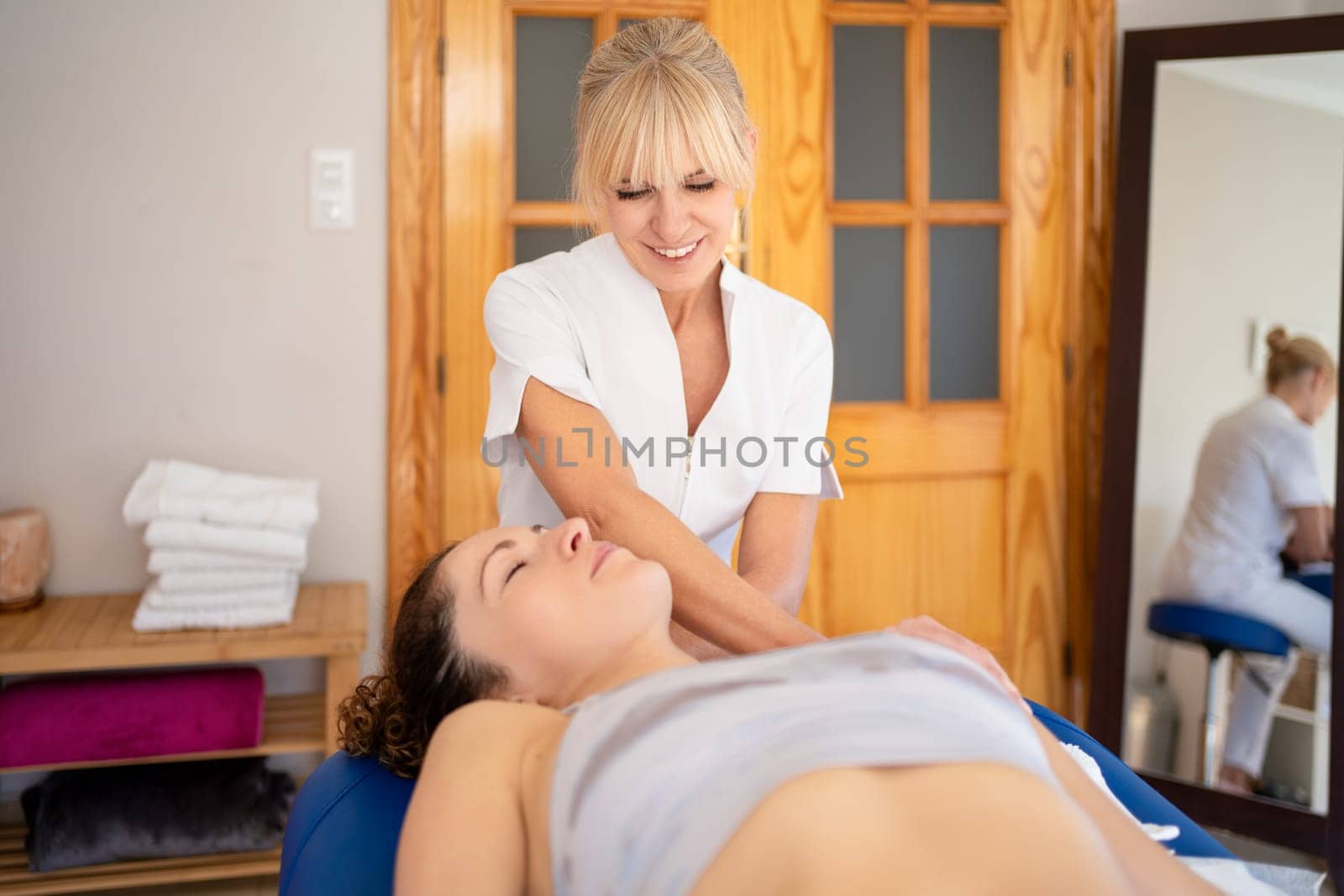 Positive female osteopath fixing neck of lying woman with hands movements during visit in manual therapy clinic